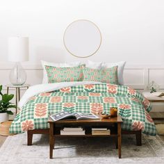 a bed with green and orange comforter next to a coffee table in front of a white wall