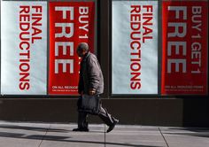 a man walking down a sidewalk past two large red and white signs on the side of a building