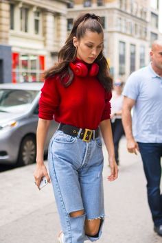 a woman walking down the street in ripped jeans and red sweater with headphones on