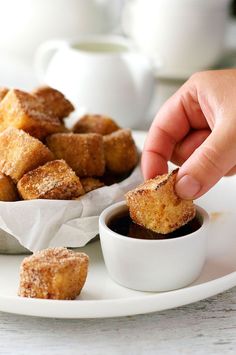 a person dipping some food into a small white bowl filled with chocolate sauce and sugar cubes