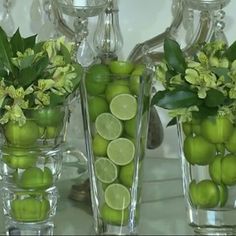 three glass vases with limes and flowers in them