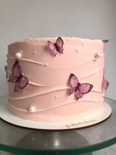 a pink cake with butterflies on it sitting on a glass platter in front of a white wall