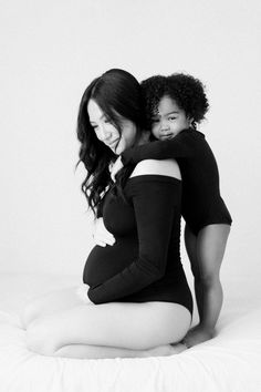 a pregnant woman sitting on top of a bed with her baby in her arms and smiling at the camera