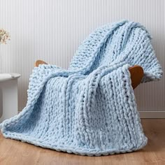 a blue knitted blanket sitting on top of a wooden chair next to a white wall