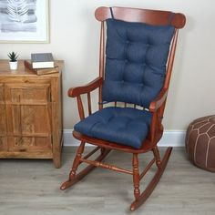 a wooden rocking chair with blue cushions in a room next to a dresser and small table