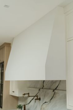 a kitchen with white cabinets and marble counter tops, including an oven hood over the stove