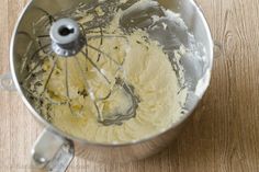 a metal mixing bowl filled with batter on top of a wooden table next to a whisk