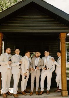 a group of men standing next to each other in front of a wooden structure holding wine glasses