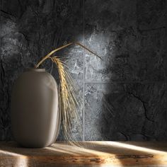 a white vase sitting on top of a wooden table next to a wall with a plant in it