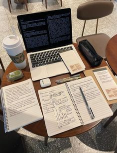 a laptop computer sitting on top of a wooden table next to notebooks and papers