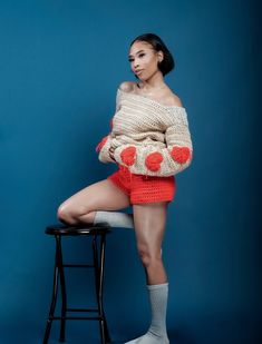 a woman sitting on top of a stool wearing an off the shoulder sweater and shorts