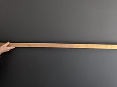 a person holding onto a wooden stick against a gray wall with their hand on it