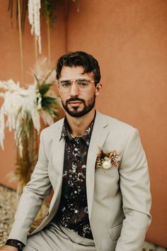 a man wearing glasses and a suit sitting on the ground next to a potted plant