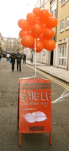 an orange sign sitting on the side of a road next to a bunch of balloons