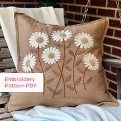 a brown pillow with white daisies on it sitting on a wooden bench next to a brick wall