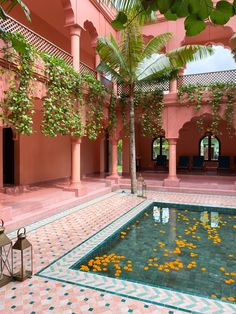 an indoor swimming pool with flowers on the ground and palm trees in the background, surrounded by tiled flooring