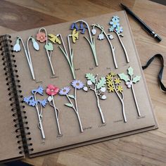 an open notebook with paper flowers on it next to a pair of scissors and pencils