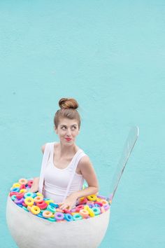 a woman sitting in a bowl filled with donuts on top of a blue wall