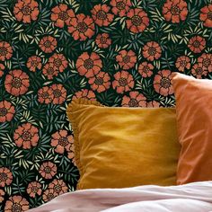 a bed topped with pillows next to a wallpaper covered in orange and green flowers