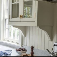 a kitchen with white cabinets and wooden cutting board in front of the window, next to a bowl of cherries