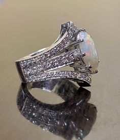 an opal and diamond ring sits on a reflective surface