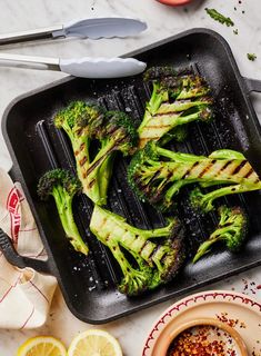 broccoli is being cooked on a grill with lemon wedges and seasoning