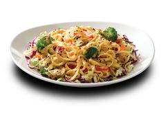 a white bowl filled with noodles and vegetables on top of a wooden table next to a fork