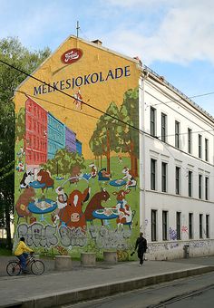 a mural on the side of a building with people riding bikes in front of it