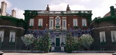 a large brick building with lots of flowers growing on it's sides and an iron gate leading to the front door