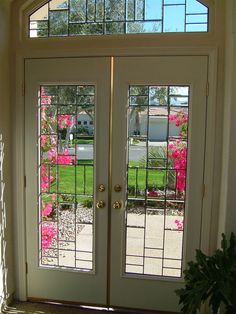 the front door to a home with two glass doors and pink flowers in the background