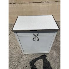 a white metal cabinet sitting on top of a cement floor next to a wall with a shadow