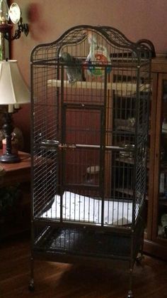 a bird cage sitting on top of a wooden floor next to a lamp and dresser