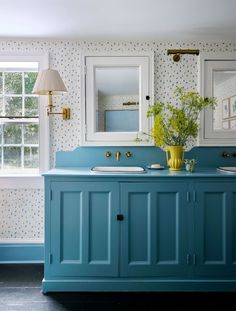 a bathroom with blue cabinets and wallpaper on the walls, two sinks and a large mirror