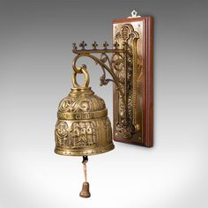 a golden bell hanging from a wall next to a wooden frame with an ornate design on it