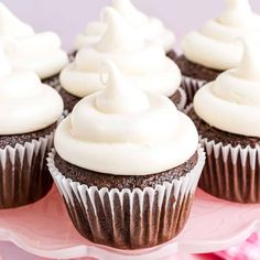 chocolate cupcakes with white frosting sitting on a pink cake platter, ready to be eaten