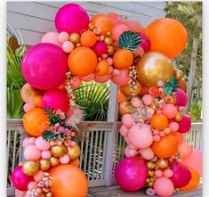 an arch made out of balloons and flowers on the front porch with palm trees in the background