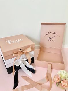 an open box with ribbon and flowers next to it on a pink tableclothed surface