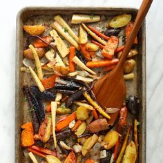 a pan filled with carrots, potatoes and other veggies next to a wooden spoon