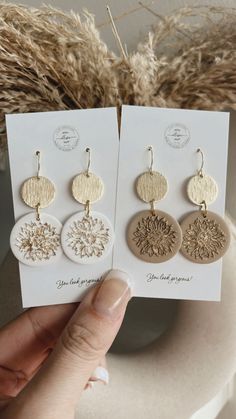 two pairs of earrings are shown in front of a white card and some dried grass