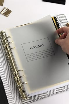 a person holding a pen and writing on a planner book next to other office supplies