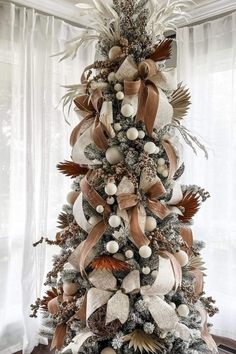 a decorated christmas tree in front of a window with white and brown decorations on it