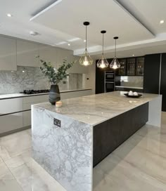 a large kitchen with marble counter tops and black cabinets, along with pendant lights hanging from the ceiling