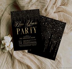 two black and gold new year's eve party cards on a bed with white flowers