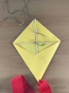 an origami kite sitting on top of a wooden table next to red ribbon