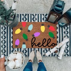 a person standing next to a door mat with the word hello written on it and decorations