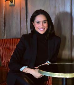 a woman sitting at a table in front of a wooden paneled wall and smiling for the camera