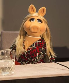 miss piggy sitting at a table with a glass of water in front of her