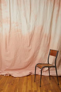 a chair sitting on top of a hard wood floor in front of a pink curtain