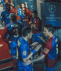 two soccer players talking to each other in front of a group of men wearing red and blue uniforms