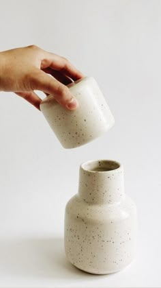 a hand is pouring something into a white ceramic vase with speckles on it